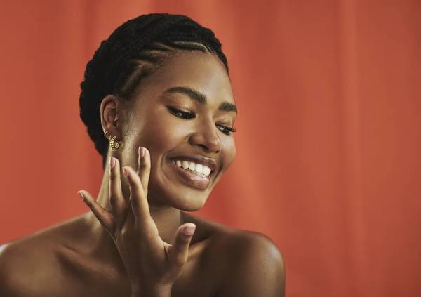 Produtos de skincare com desconto na Black Friday: uma mulher negra cuidando da pele do rosto em um fundo vermelho.